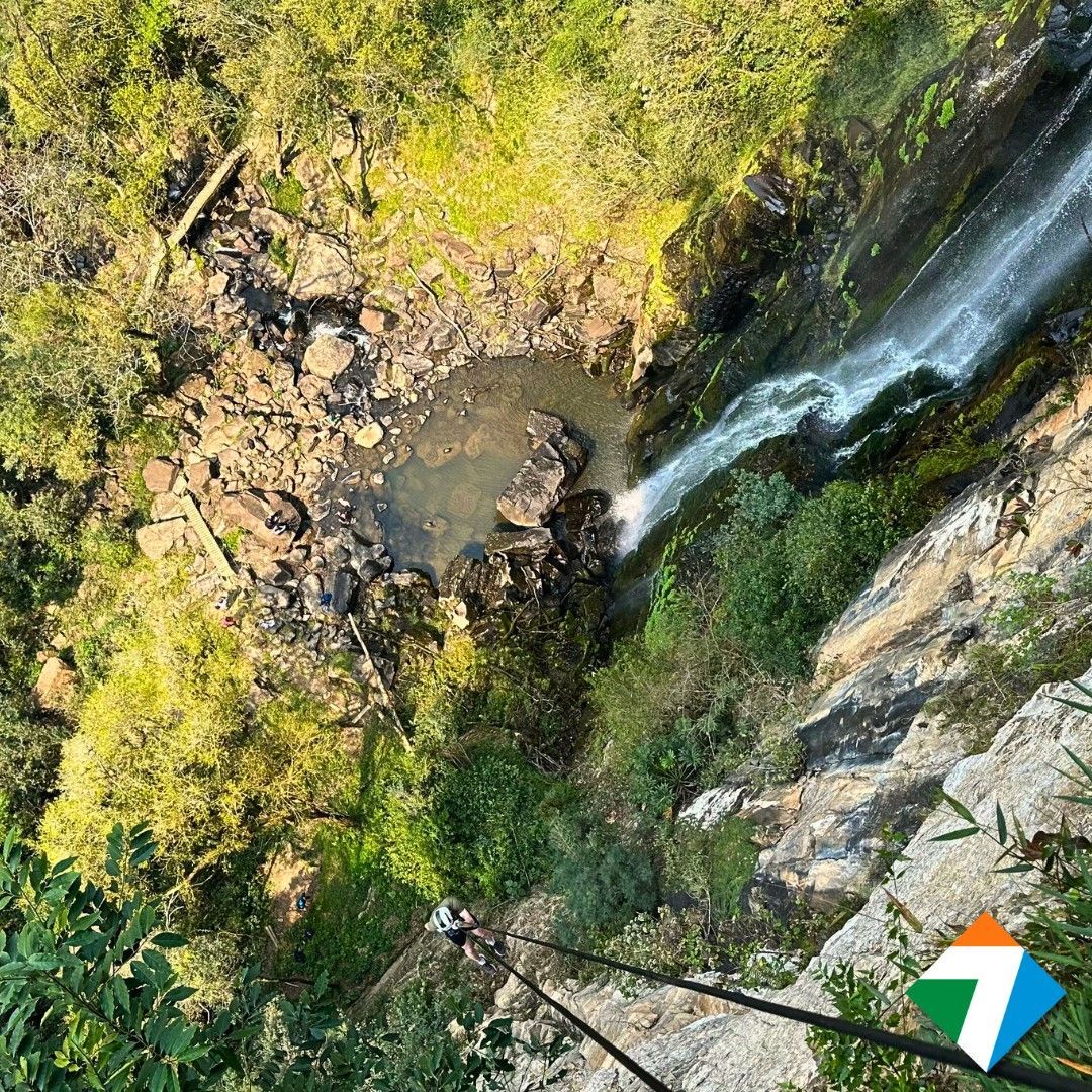 Pessoa praticando rapel em uma cachoeira; uma exuberante floresta verde circunda a queda d'água.