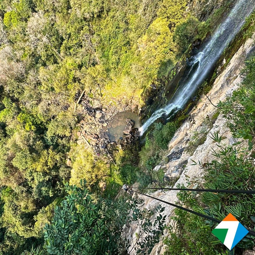 Cachoeira despencando pela encosta do penhasco. Floresta verdejante ao redor. Duas cordas em primeiro plano.