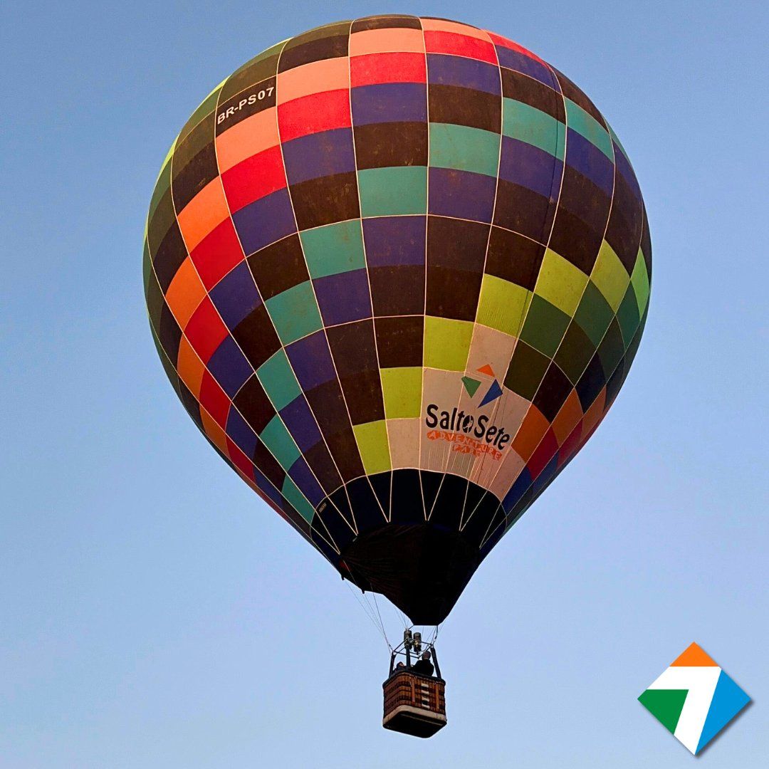 Um balão de ar quente colorido em voo contra um céu azul, com passageiros na cesta.