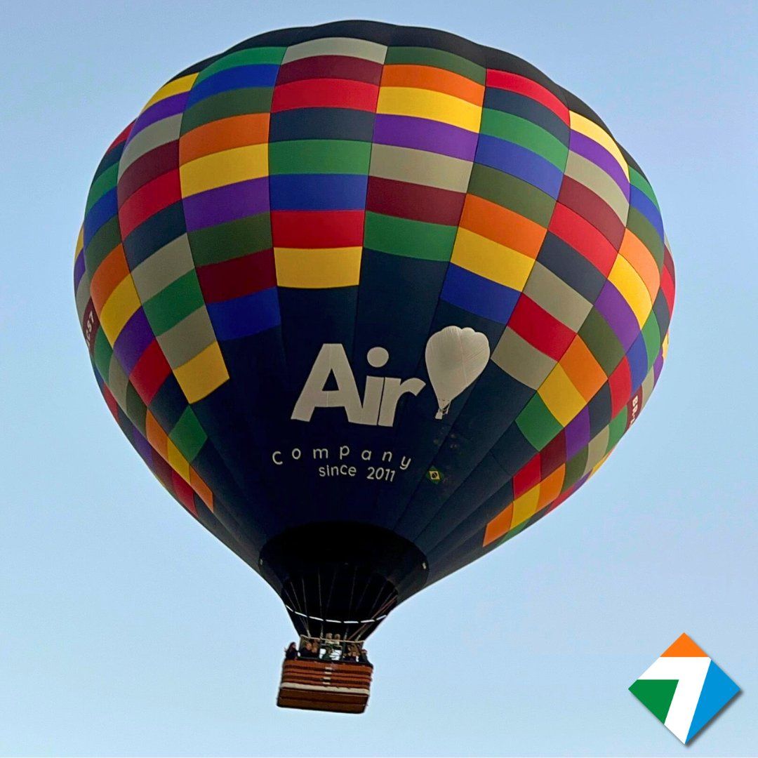 Um balão de ar quente colorido em voo contra um céu azul, exibindo a inscrição