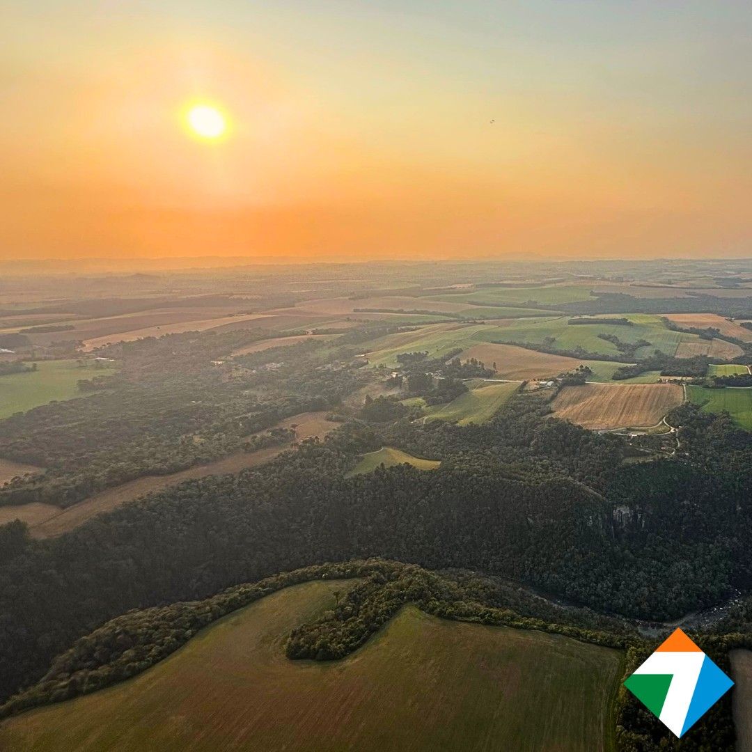 Pôr do sol sobre uma paisagem com campos, florestas e um sol brilhante.