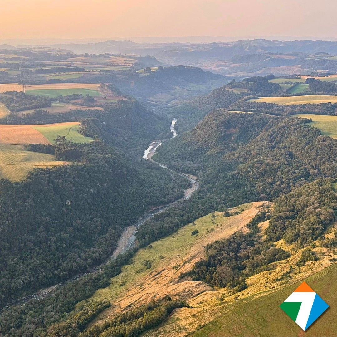 Vista aérea de um vale com um rio serpenteando por uma exuberante floresta verde e colinas onduladas ao redor.