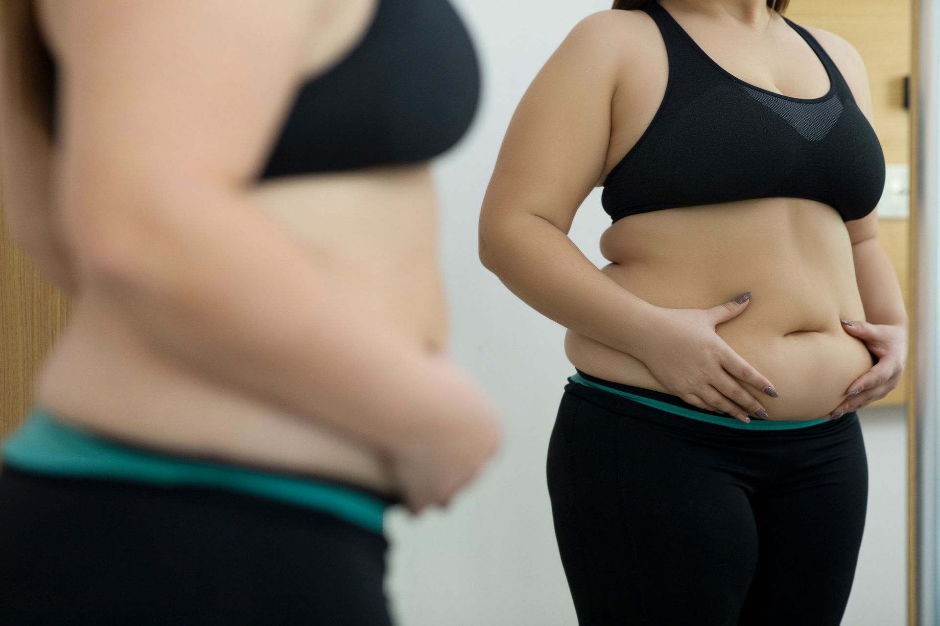 A Woman Is Looking at Her Stomach in The Mirror — LaGrange, GA — LaGrange Body Lab