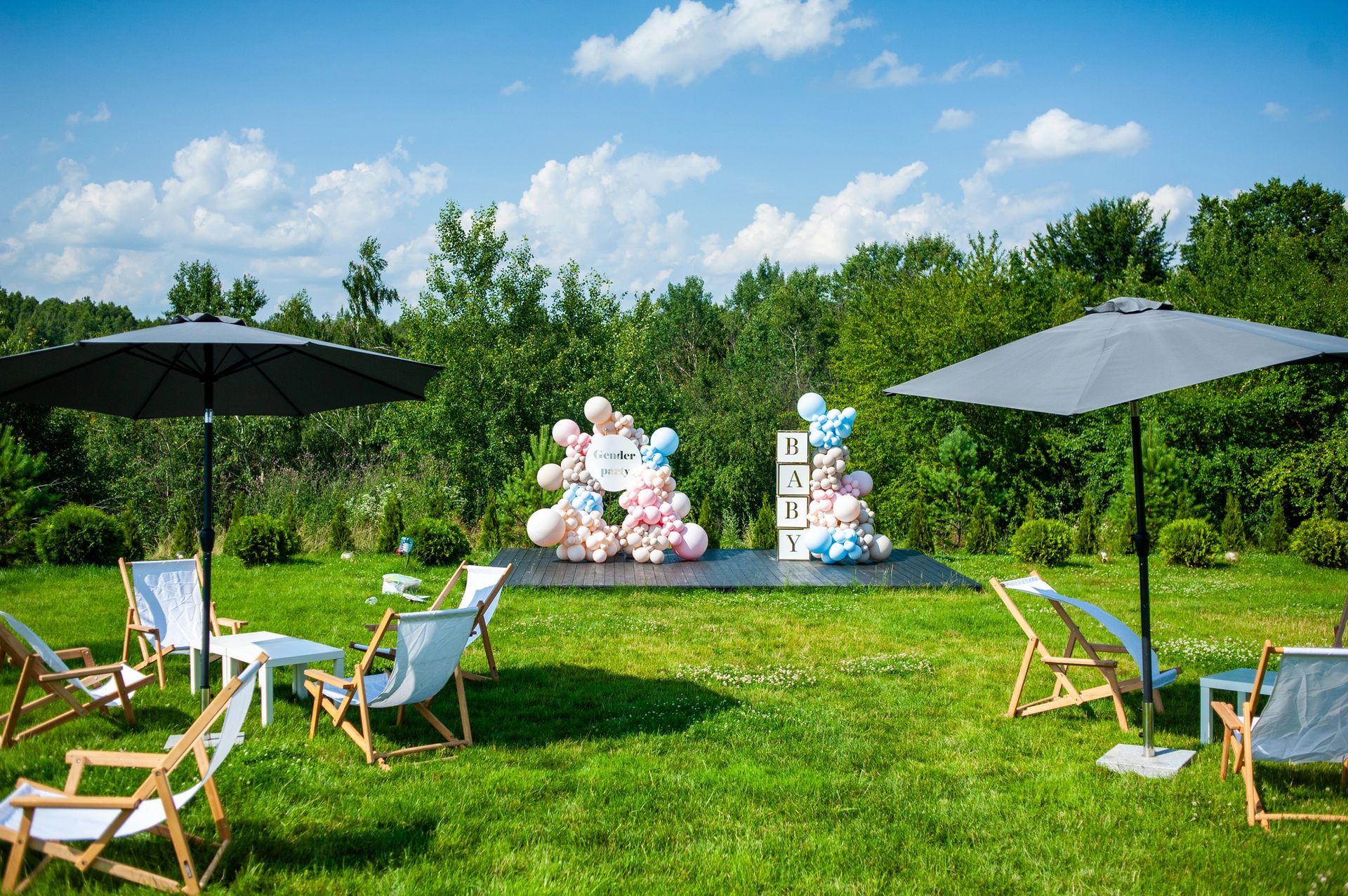 Allestimento per festa con palloncini blu e bianchi, tavolo decorato e torta in una stanza illuminata da luci soffuse.