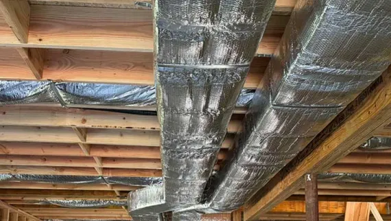 Insulated HVAC ducts wrapped in silver foil installed in a wood-framed ceiling.