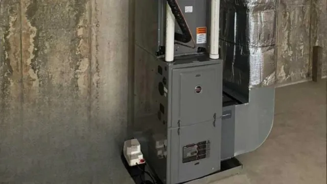 A gray furnace in a basement setting with ductwork and a white pipe.