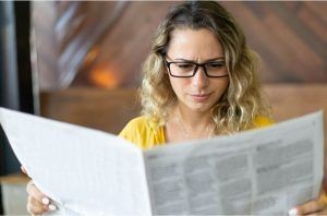 A woman wearing glasses is reading a newspaper.