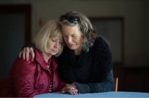 Two women are sitting at a table hugging each other.