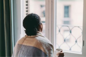 A woman is looking out of a window while holding a cup of coffee.