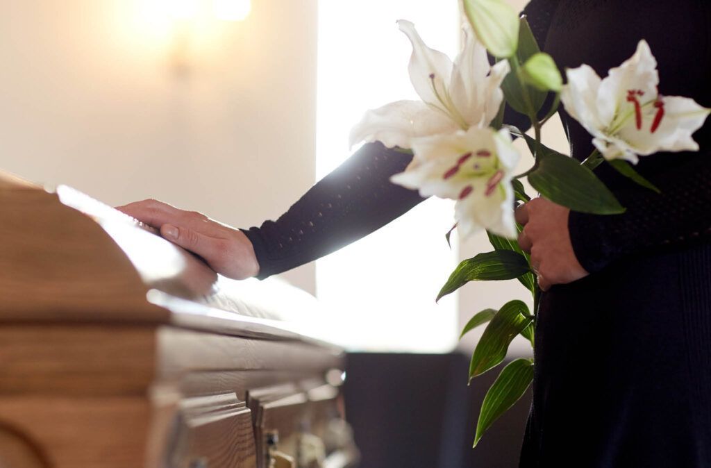 A woman is holding flowers in front of a coffin at a funeral.