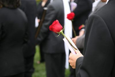 A man is holding a red rose at a funeral.