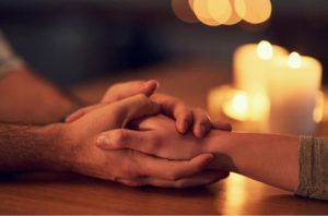 A man and a woman are holding hands at a table with candles in the background.