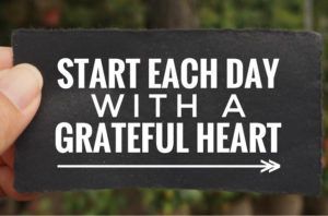 A person is holding a sign that says start each day with a grateful heart