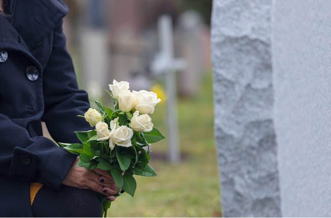 A woman is holding a bouquet of white roses in front of a grave.