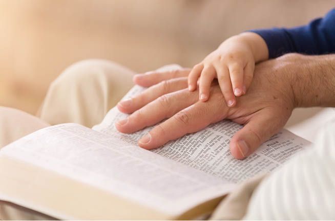 A man and a child are holding hands over a bible.