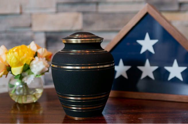 A black urn is sitting on a table next to an american flag.