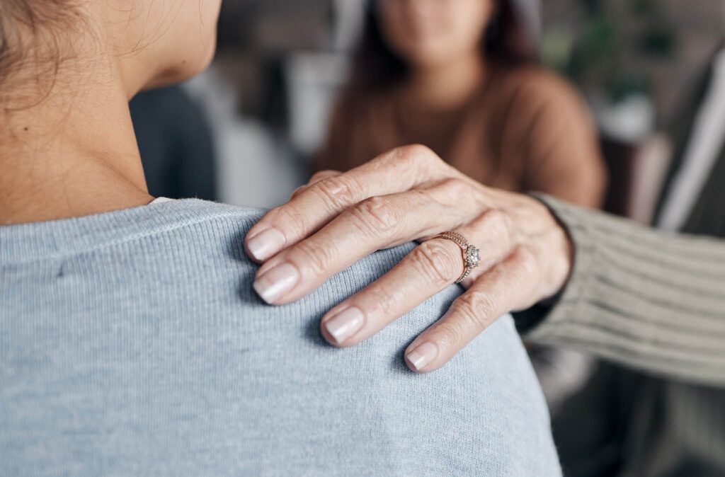 A woman is putting her hand on another woman 's shoulder.