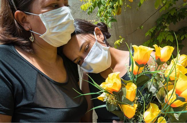 Two women wearing face masks are looking at a bouquet of yellow flowers.