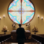 A man is standing in front of a stained glass window in a church.