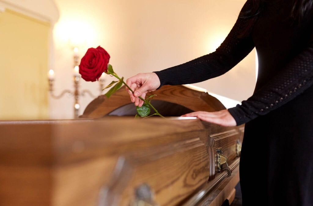 A woman is putting a red rose into a coffin at a funeral.