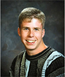 A young man wearing a sweater smiles for the camera