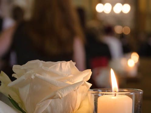 A white rose is sitting next to a lit candle in a glass.