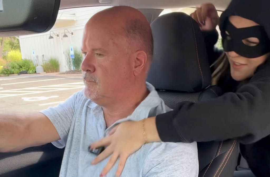 Masked woman leans from the back seat over a man driving, showing how grief tries to take the wheel
