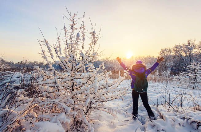 A woman is standing in the snow with her arms in the air.