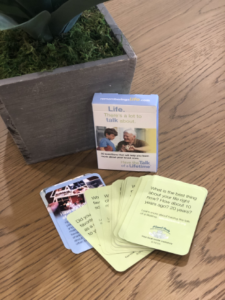 A box of cards is sitting on a wooden table next to a potted plant.