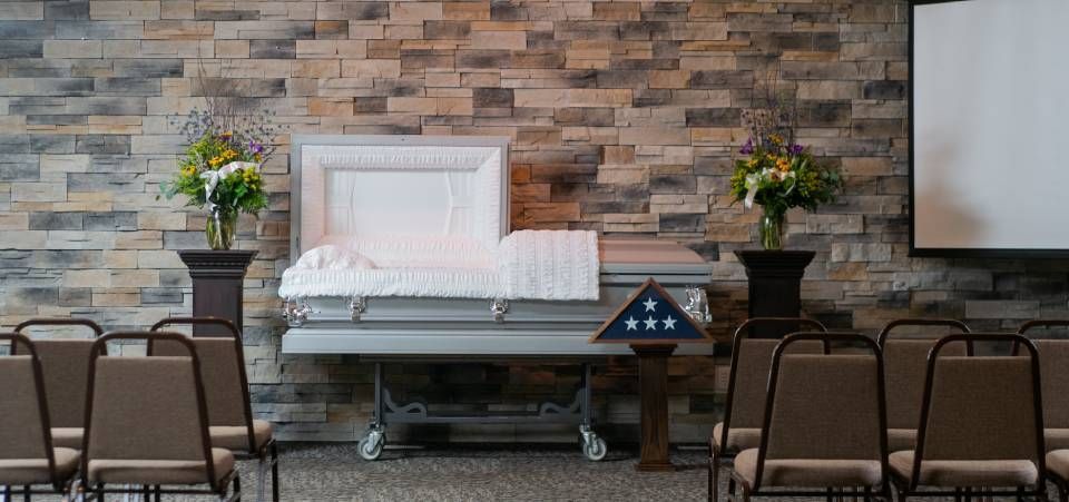There is a coffin in the middle of a room with chairs.