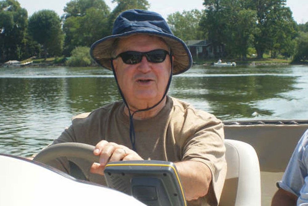 A man wearing a hat and sunglasses is driving a boat