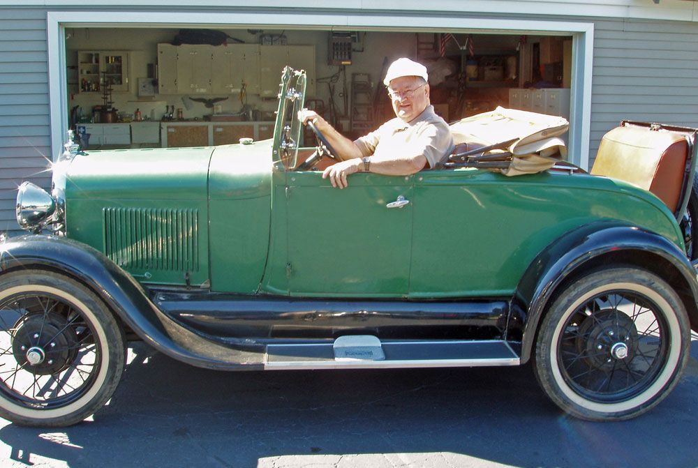 A man is sitting in a green car in front of a garage door