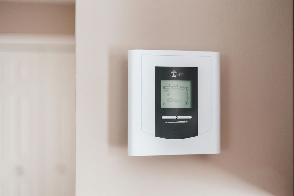 White thermostat on a pale pink wall with a blank, slightly open door to the left.