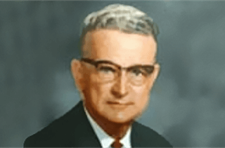 A man with glasses and a mustache is wearing a suit and tie