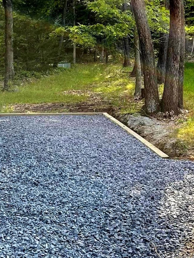 A gravel driveway in the middle of a forest with trees in the background by Tailored Excavation.