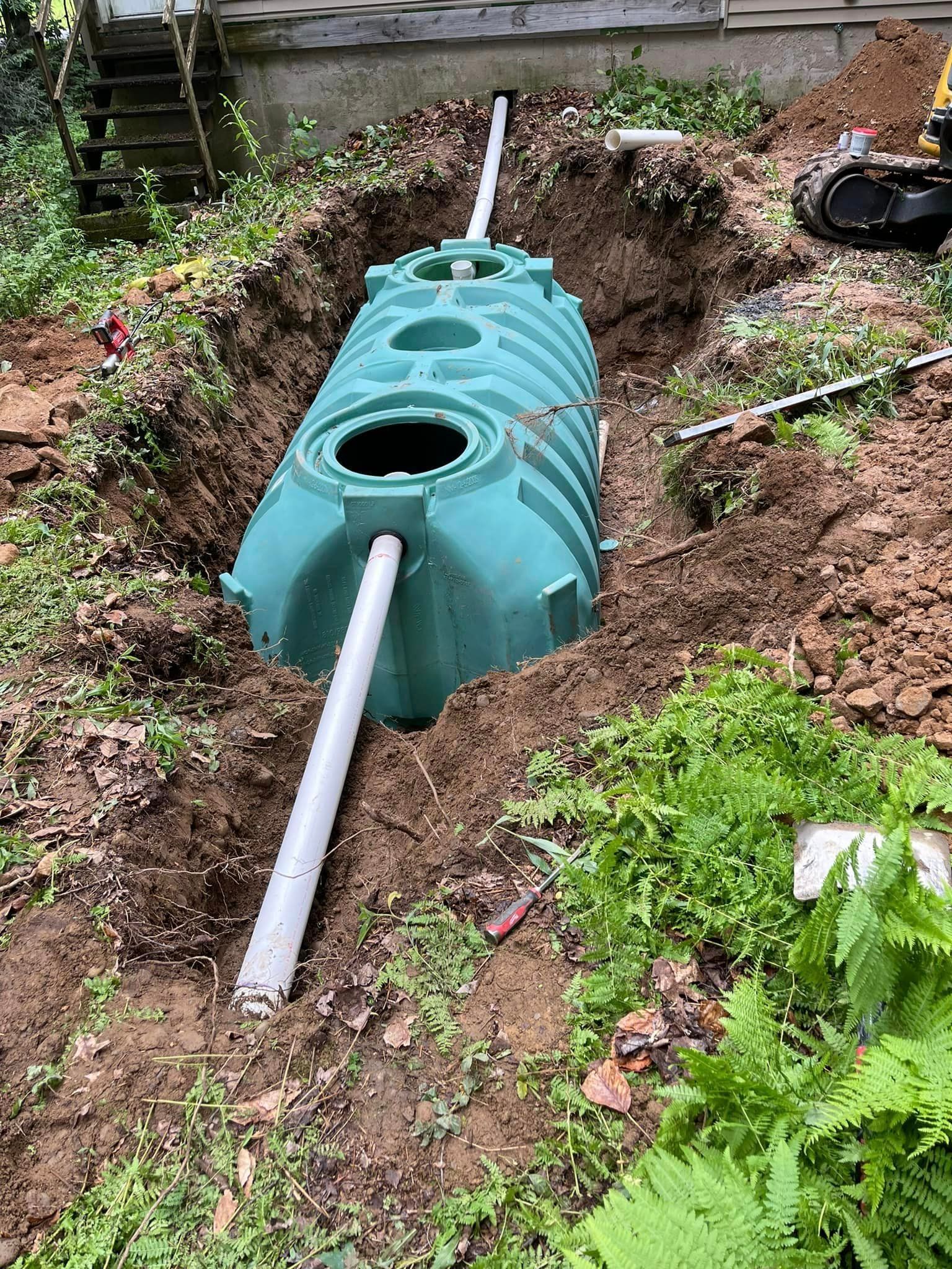 A green septic tank is being installed by Tailored Excavation in a hole in the ground.
