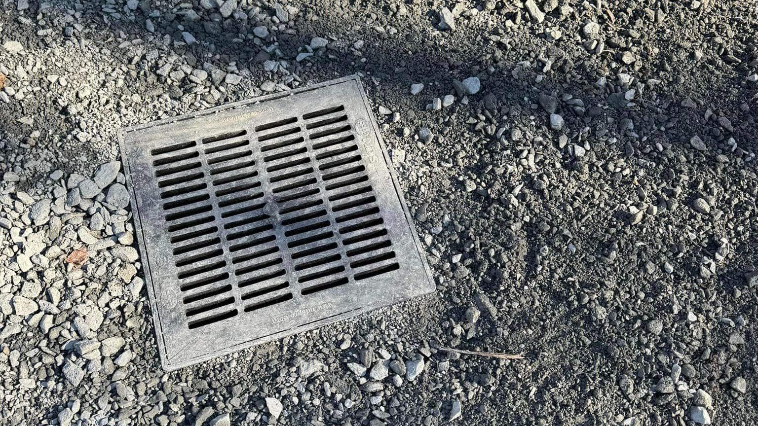 A manhole cover is sitting on top of a pile of gravel by Tailored Excavation.