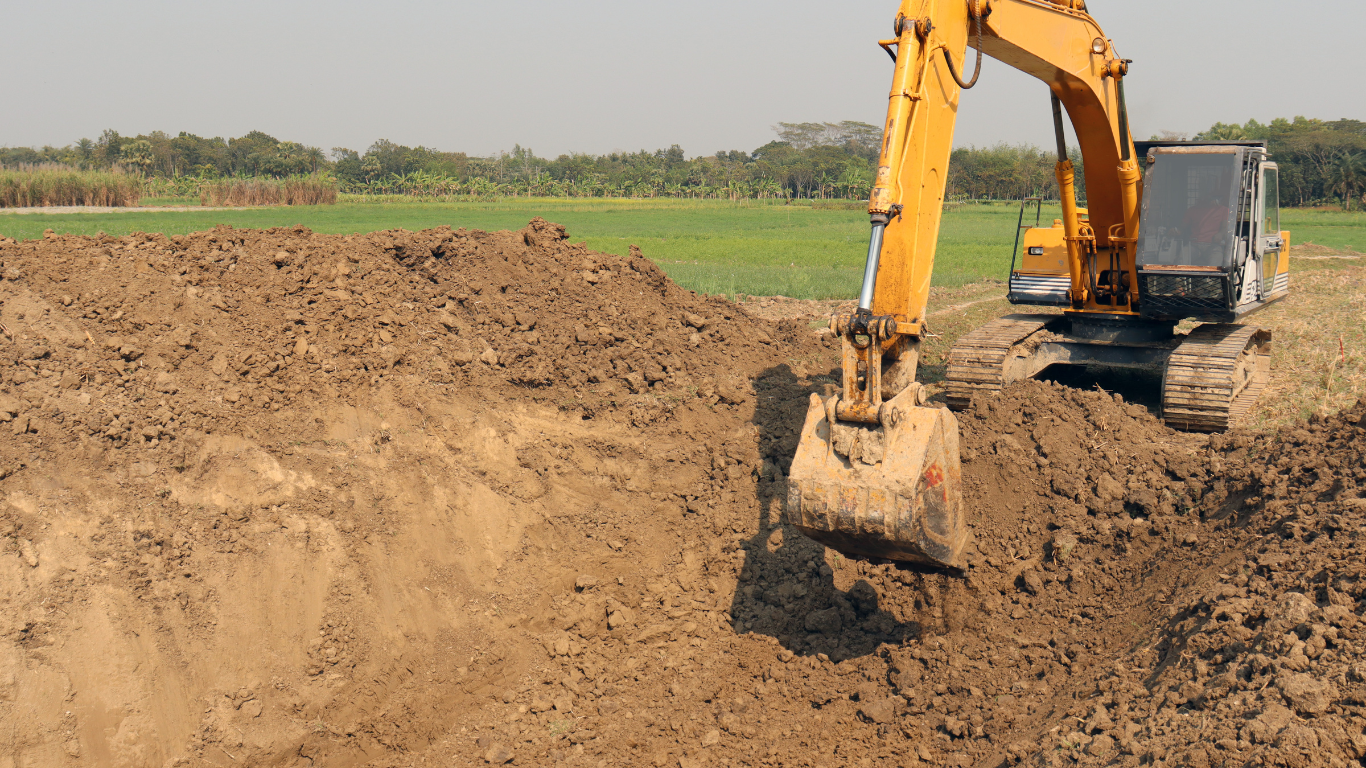 A yellow excavator is digging a hole in a field.