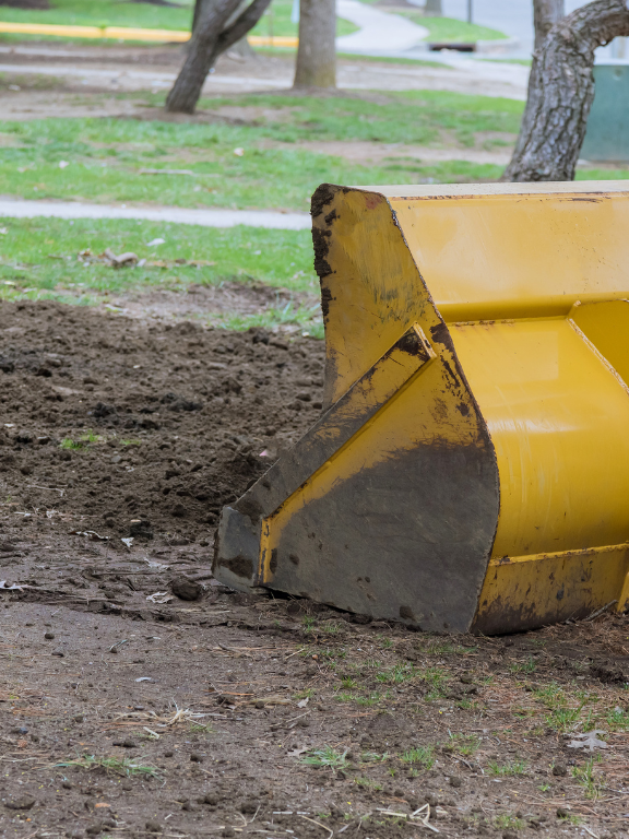 A yellow Tailored Excavation bulldozer is sitting in the dirt in a park.