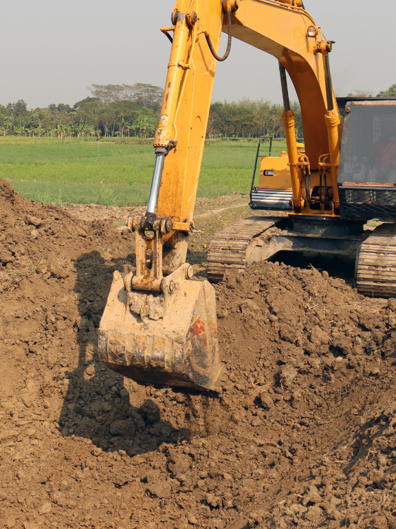 A yellow excavator is digging a hole in the dirt in a field.
