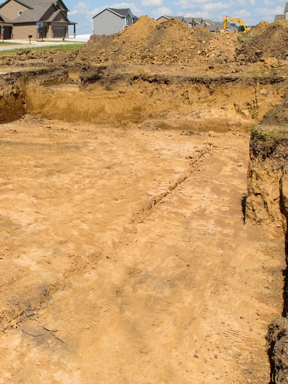 A construction site with a pile of dirt and a house in the background.