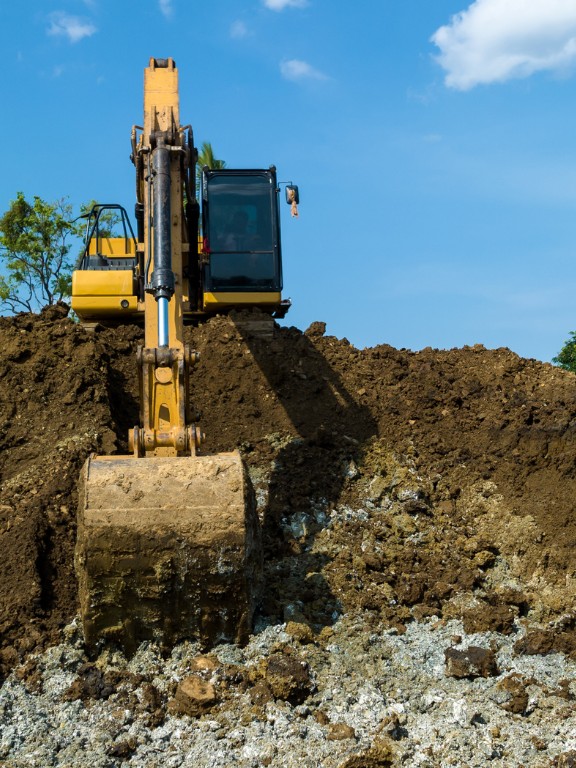 A yellow excavator is digging a hole in a pile of dirt.