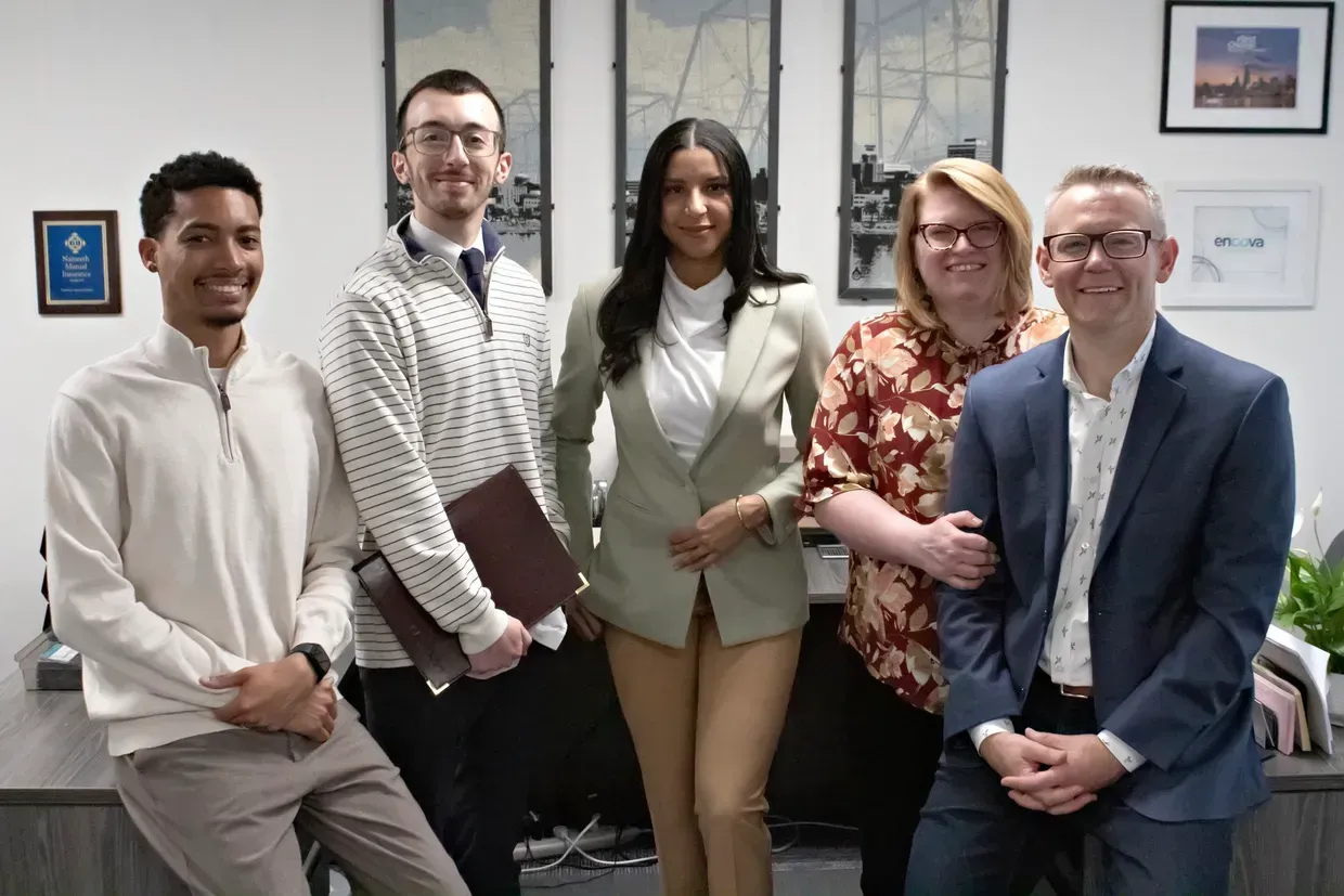 Five people posing together in an office hallway, standing close and smiling
