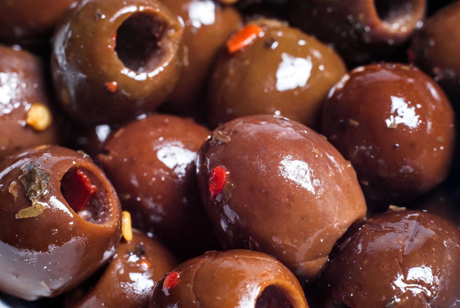 Primo piano di olive snocciolate, di colore marrone scuro, ripiene di peperoni rossi.