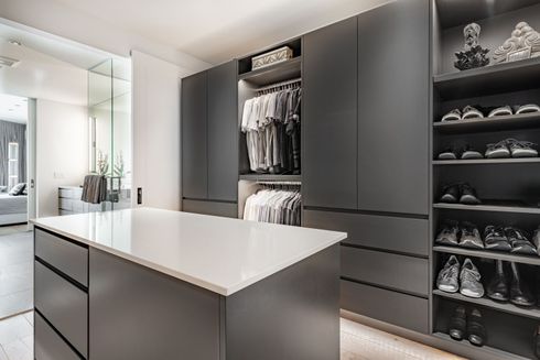 Modern walk-in closet with gray cabinets, open shelves, and a white island countertop