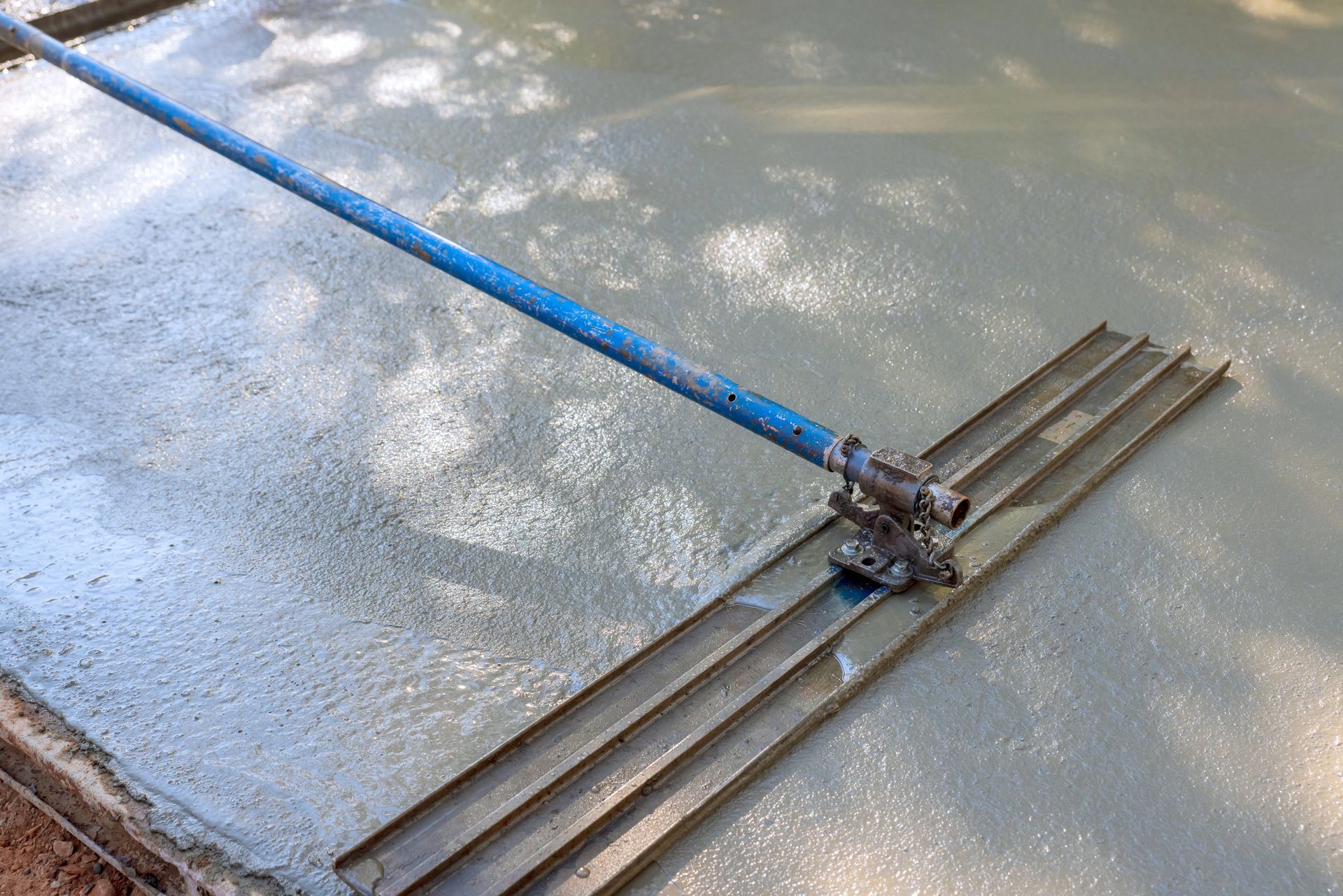 Leveling fresh concrete with a long handled tool on a sunny day.