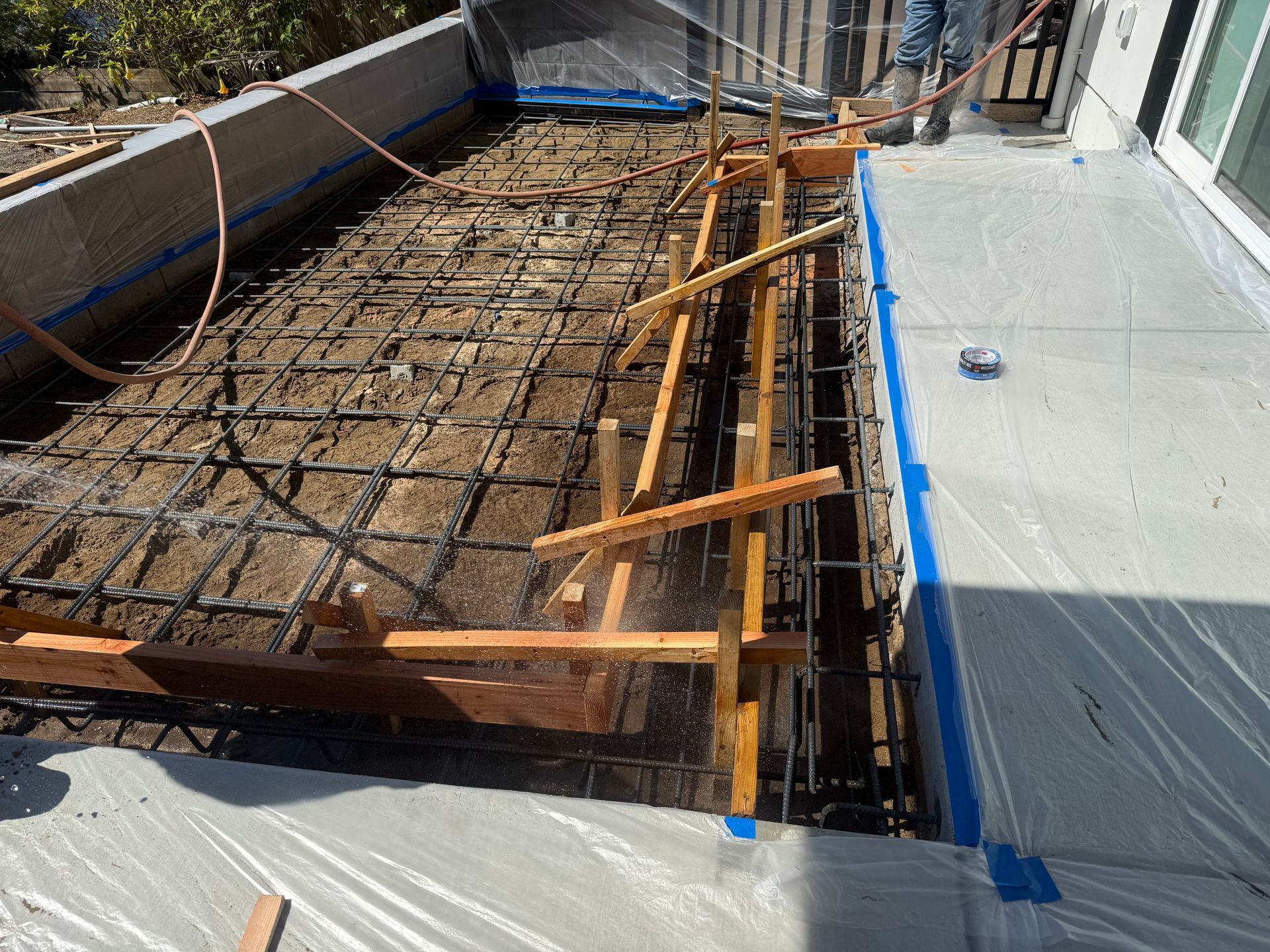 Construction site with concrete forms, rebar grid, wooden supports, and a person pouring concrete.
