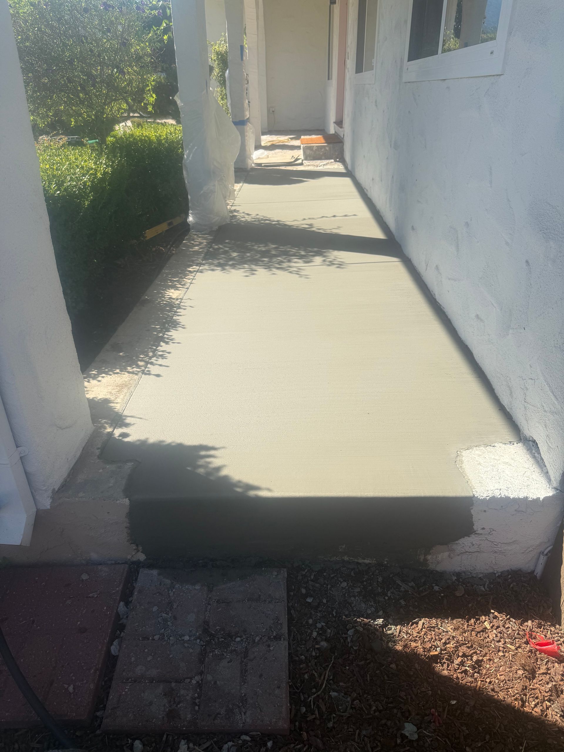 Newly poured concrete walkway and step along a white building with pillars.