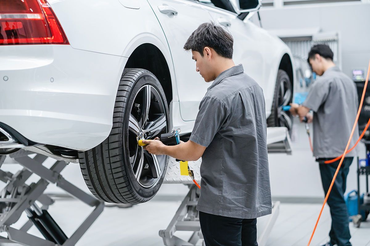 Mechanic checking a white car’s rear wheel in a bright auto repair shop