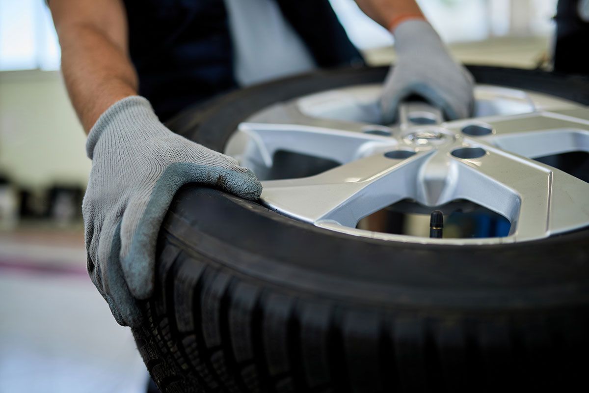 Gloved hands fitting a car tire onto a silver alloy wheel in a repair shop